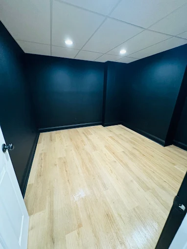 Empty room with light wood flooring, black walls, a white ceiling with recessed lights, and a partially open white door.